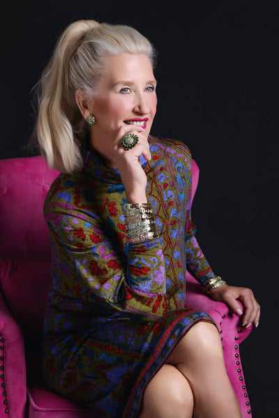 Woman in a colorful dress sitting on a pink chair against a black background