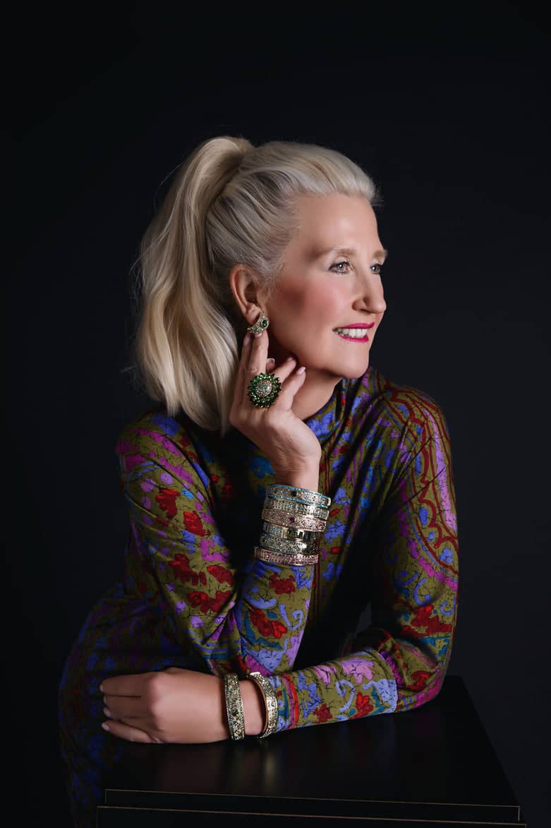 Woman wearing a colorful patterned top with jewelry against a black background