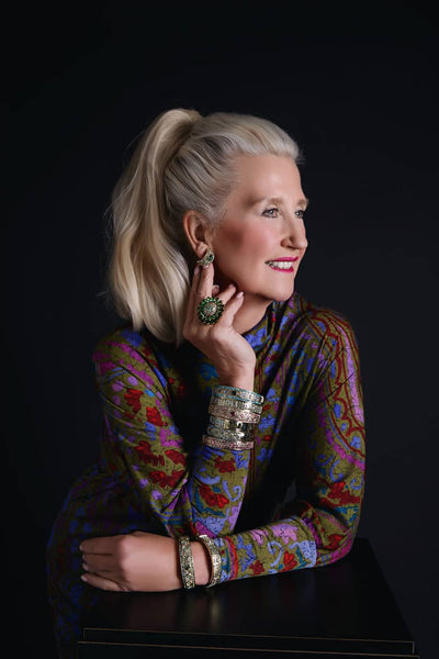 Woman wearing a colorful patterned top with jewelry against a black background