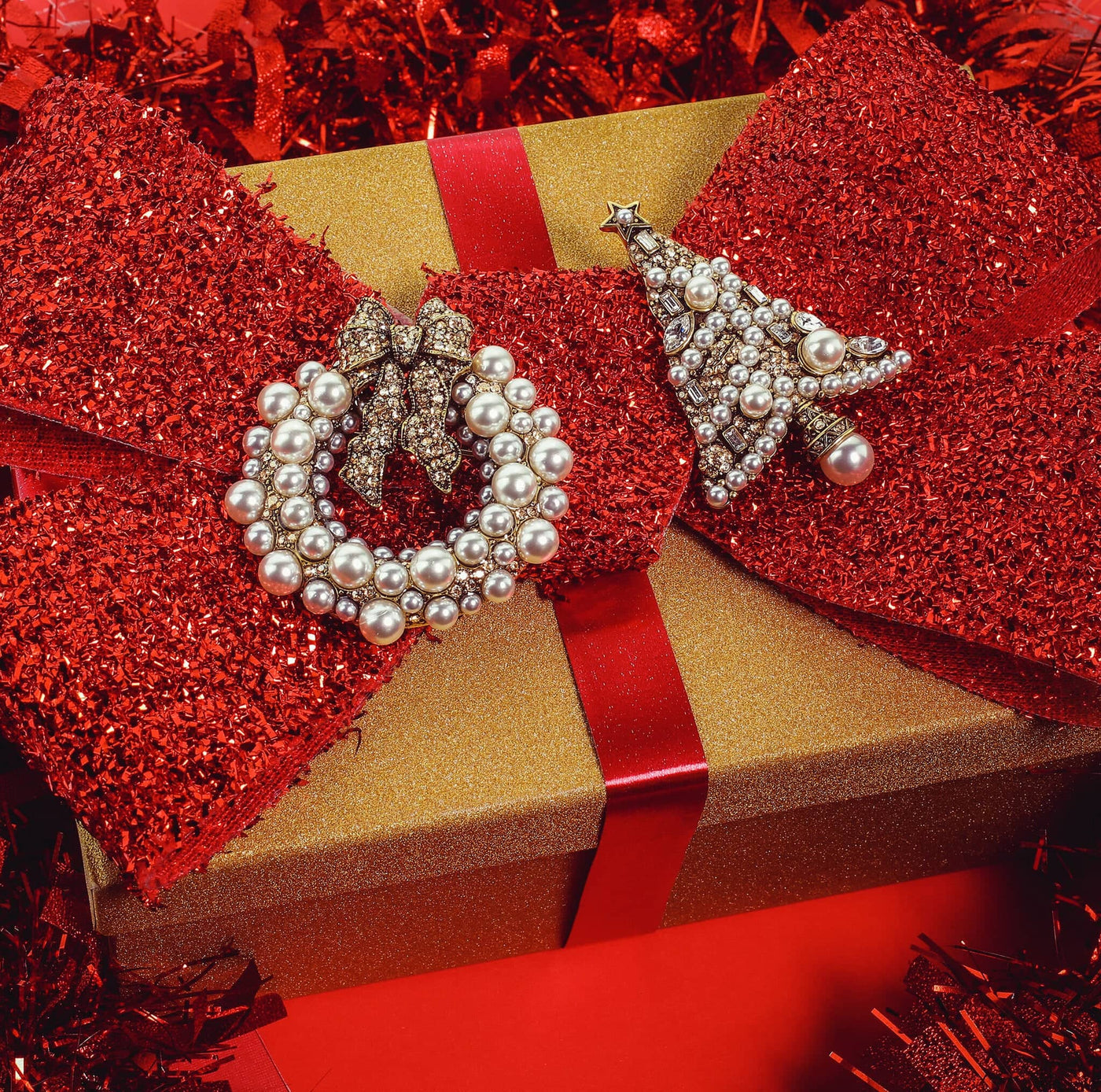Gold gift box with red glittery bow and pearl-encrusted earrings on a red background