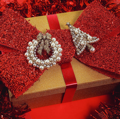 Gold gift box with red glittery bow and pearl-encrusted earrings on a red background