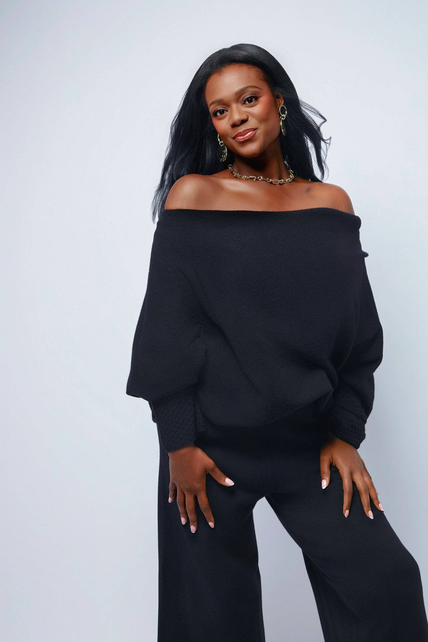 Woman wearing a black off-shoulder top and black pants against a light gray background