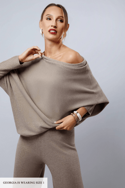 Woman wearing a beige off-shoulder top and pants against a light gray background