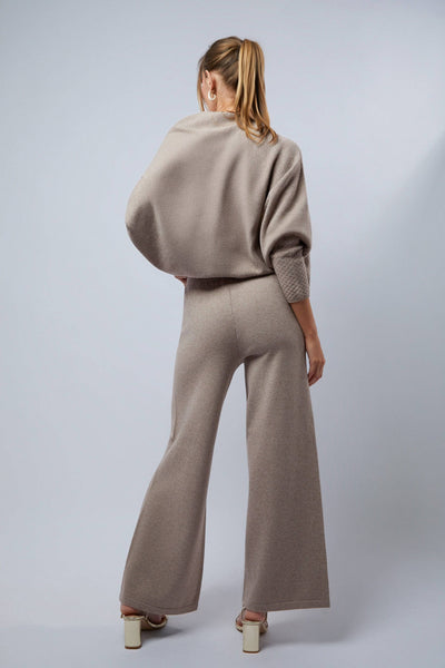 Woman wearing a beige outfit with wide-leg pants on a light gray background