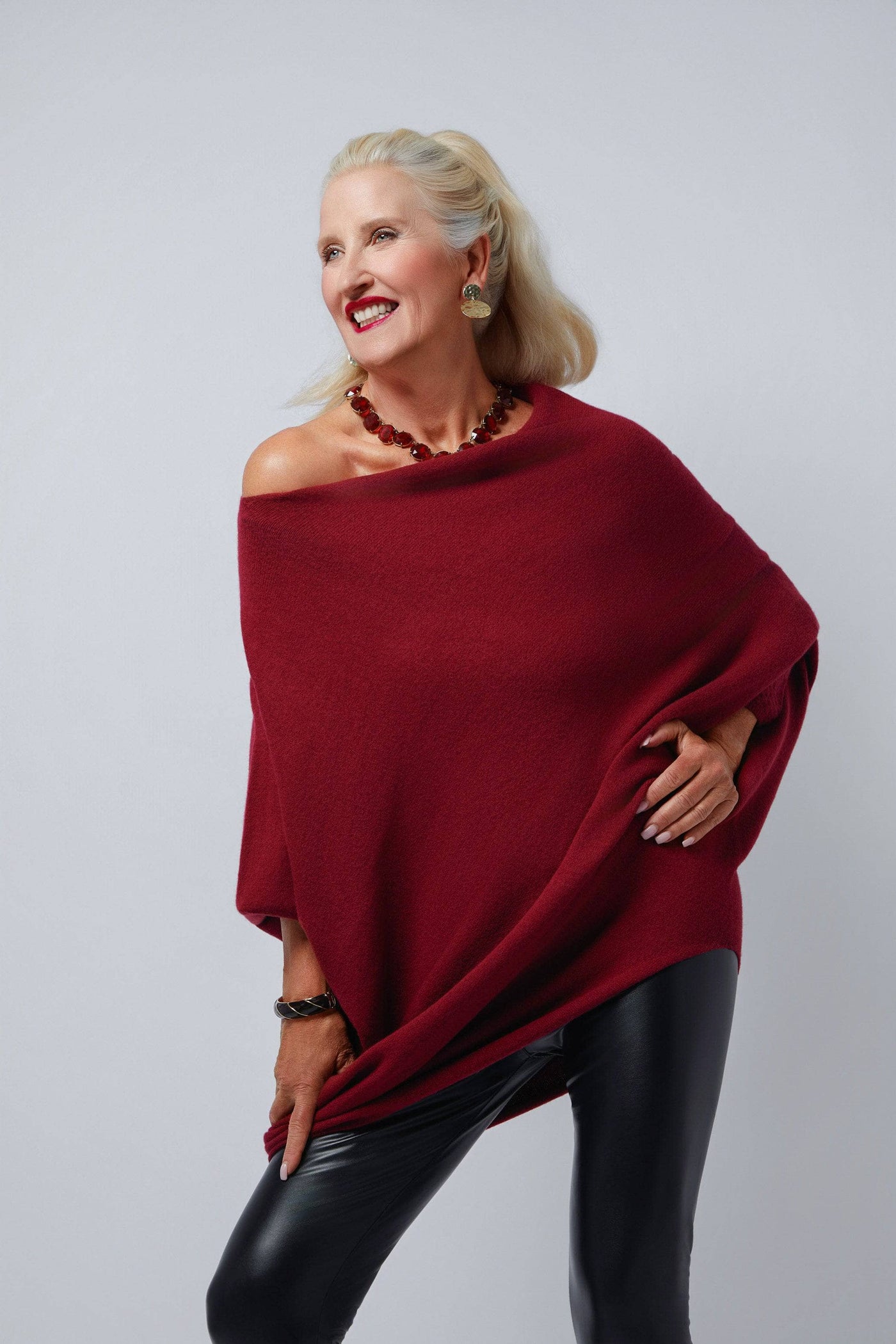Woman wearing a red poncho and black pants against a gray background