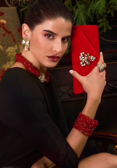 Woman holding a red clutch with decorative elements, wearing matching jewelry.