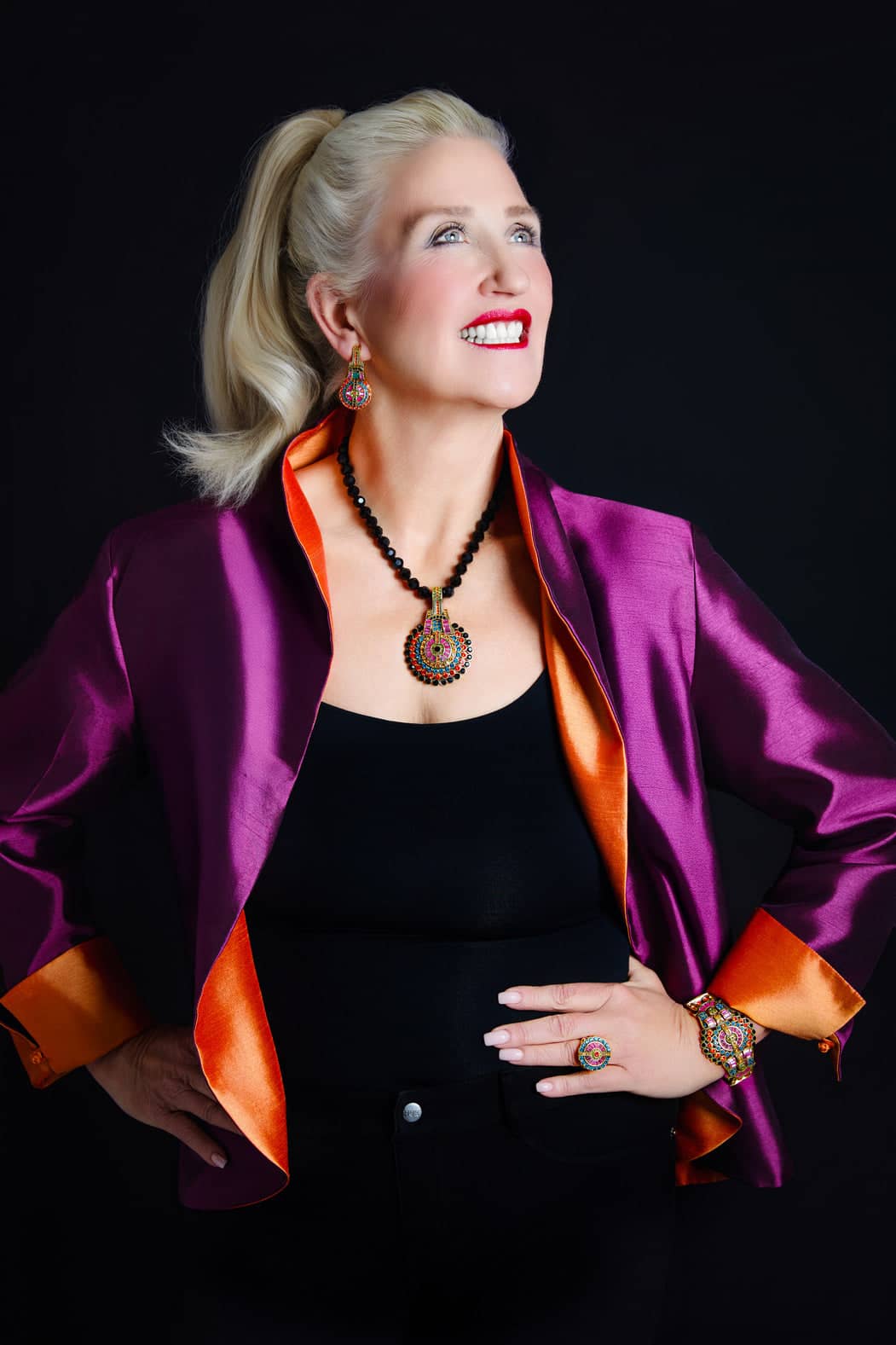 Woman wearing a purple jacket with orange accents and a black top against a dark background