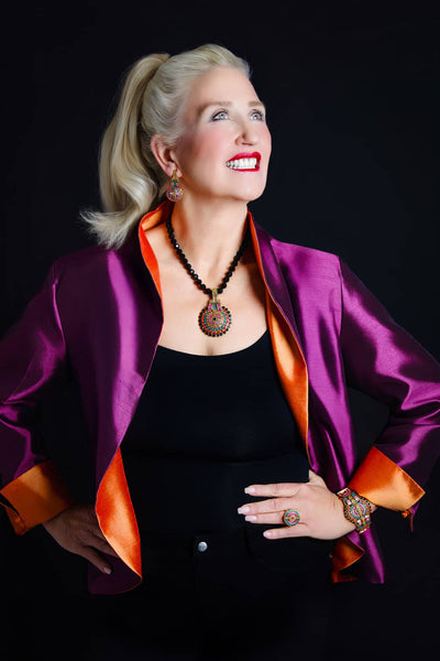 Woman wearing a purple jacket with orange accents and a black top against a dark background