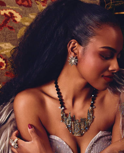 Woman in a costume with intricate designs and jewelry, surrounded by mirrors.