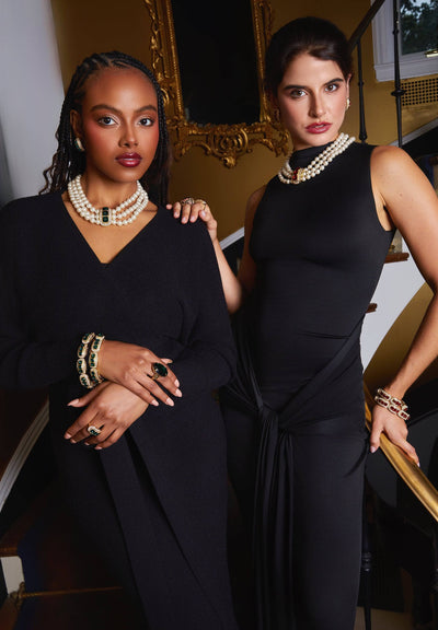 Two women in formal attire standing close together with a decorative mirror in the background.