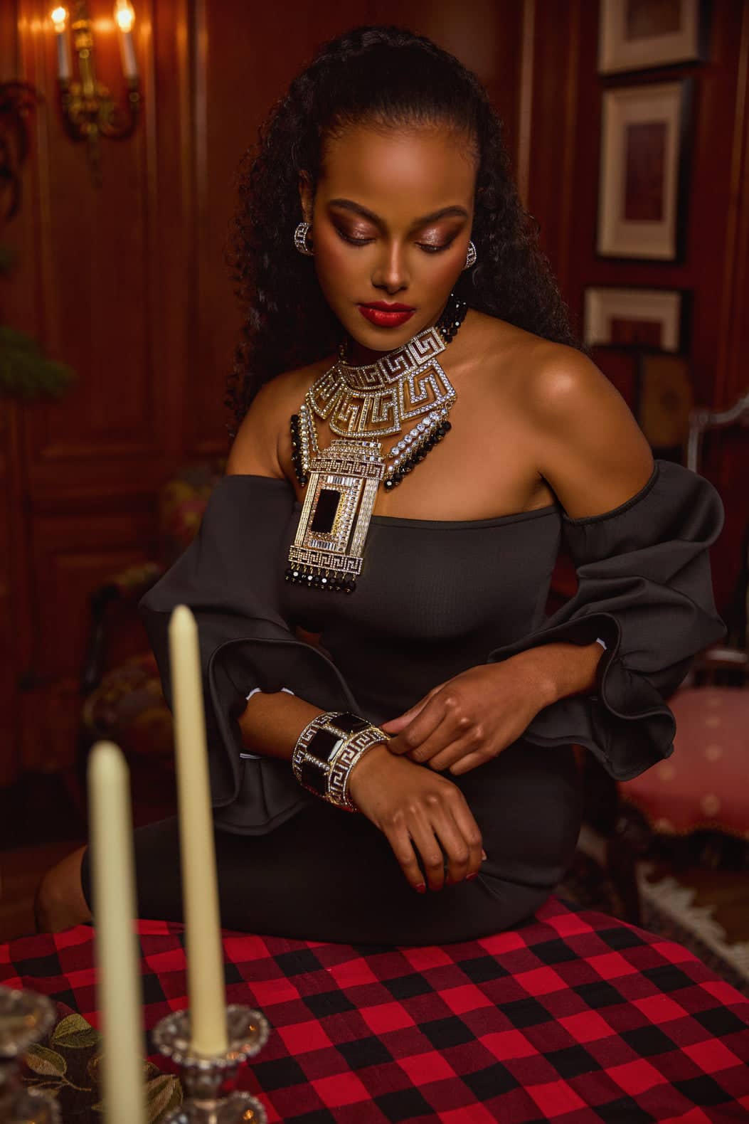 Woman in a black outfit with large jewelry sitting at a table with candles and a checkered tablecloth.