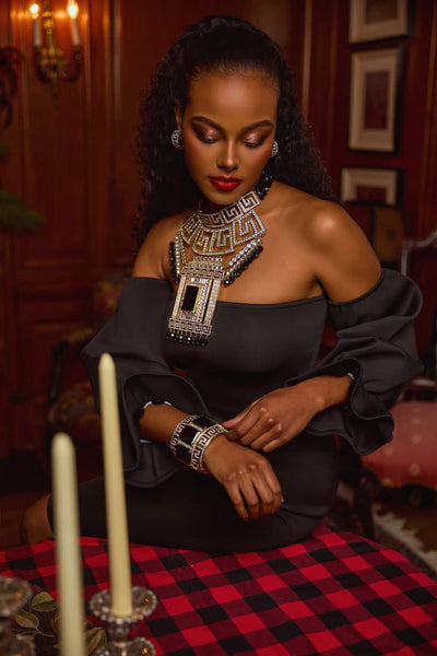 Woman in a black outfit with large jewelry sitting at a table with candles and a checkered tablecloth.