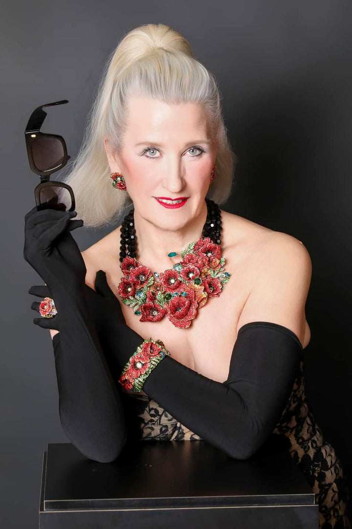 Woman with floral jewelry and black gloves holding sunglasses against a dark background