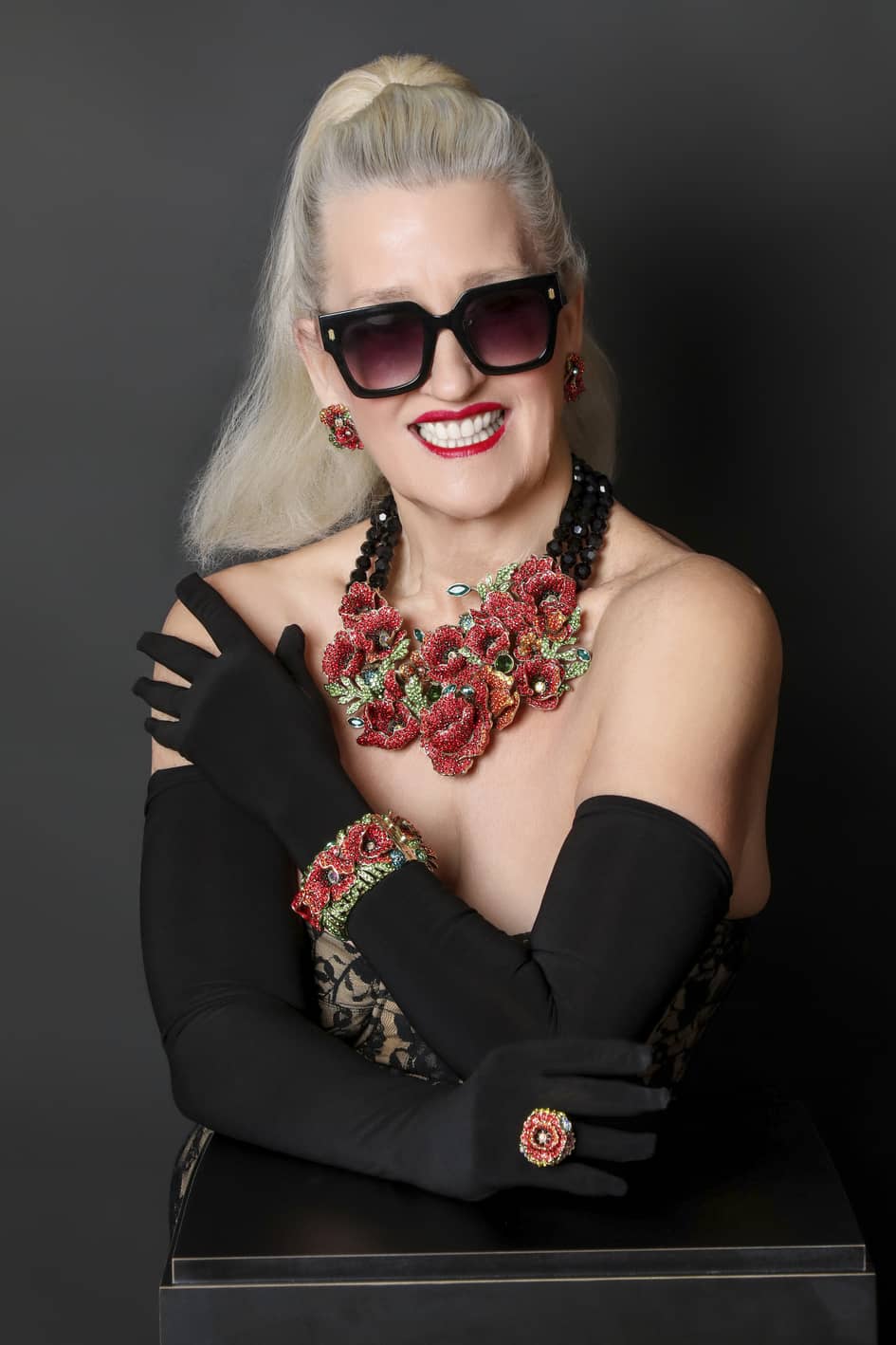 Woman wearing a floral necklace and black gloves against a dark background