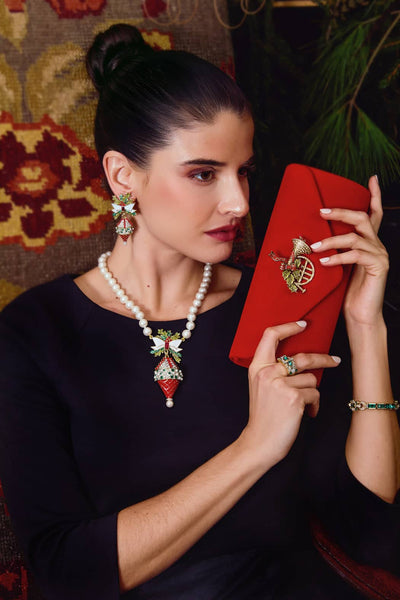 Woman holding a red clutch with intricate design, wearing a black top and jewelry.