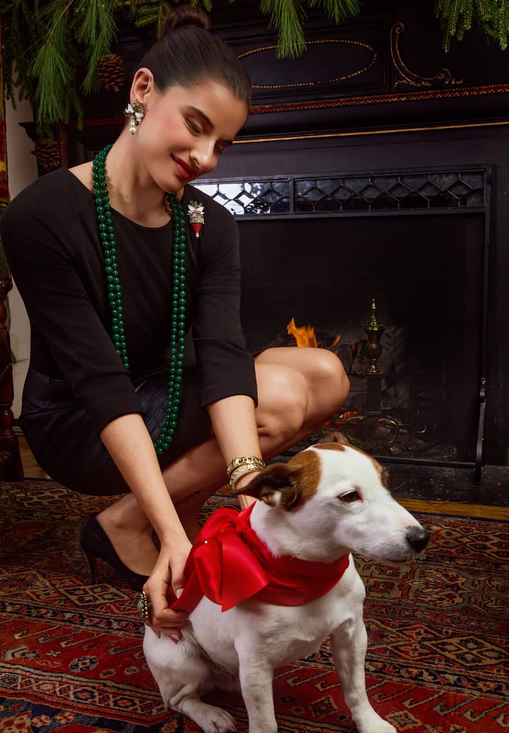 Woman with a dog wearing a red bow tie in a cozy room with a fireplace.