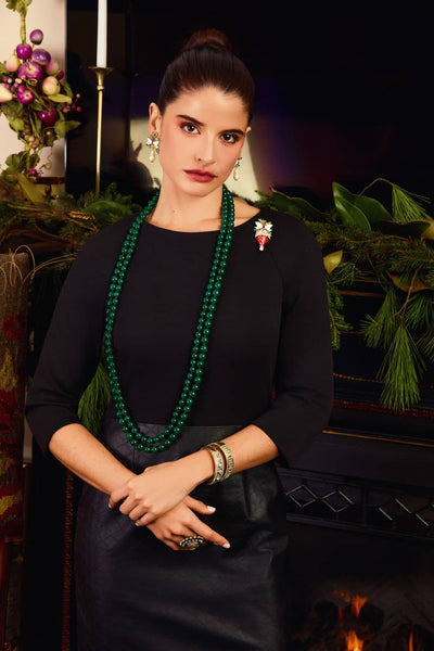 Woman wearing a black dress with a green beaded necklace in front of a decorated fireplace.