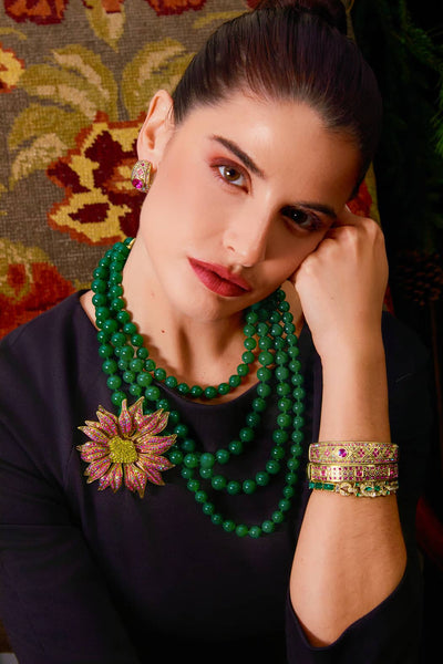 Woman wearing a green beaded necklace and bracelet with a floral earring against a patterned background
