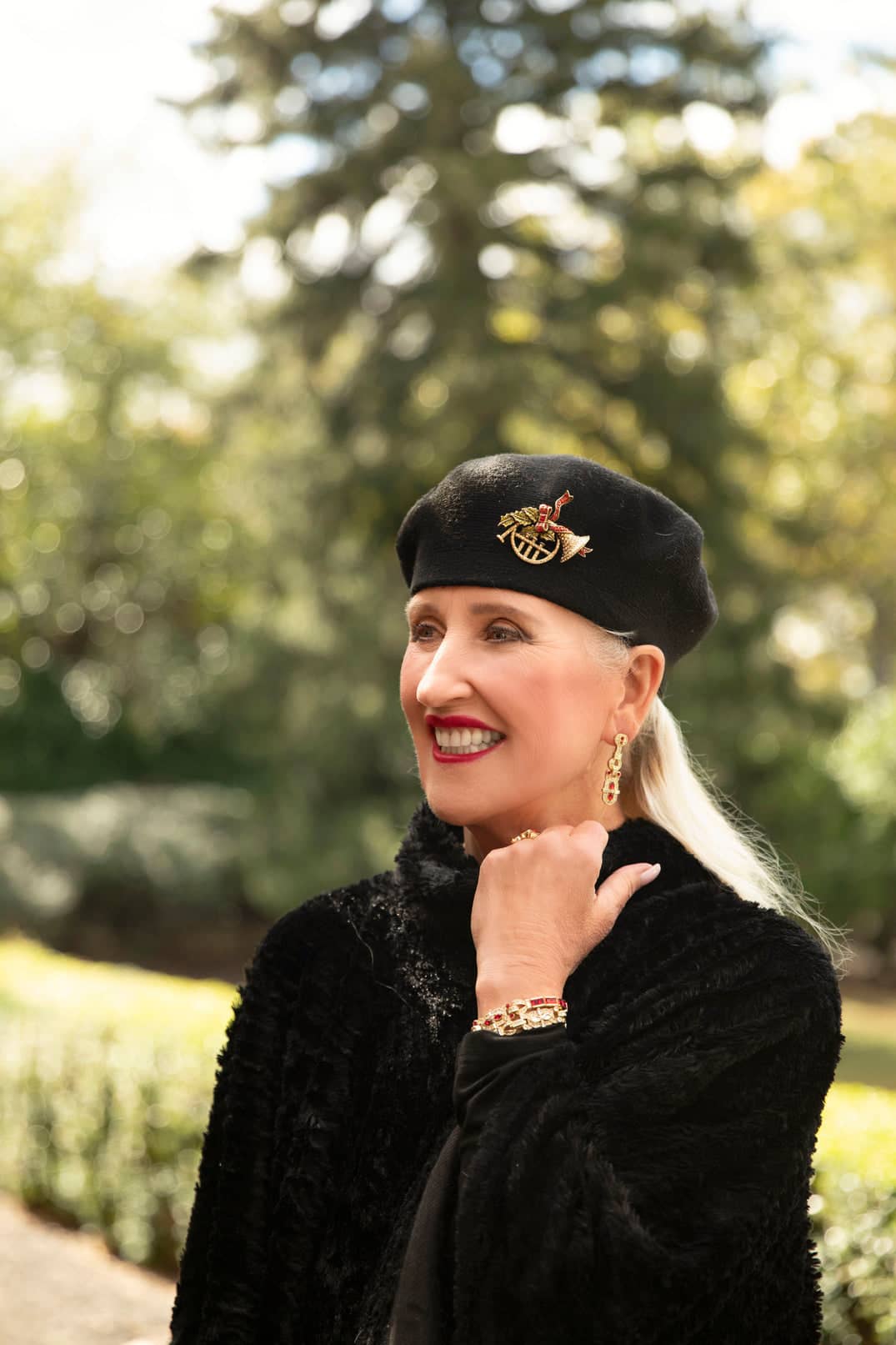 Woman wearing a black beret with a badge, smiling outdoors.