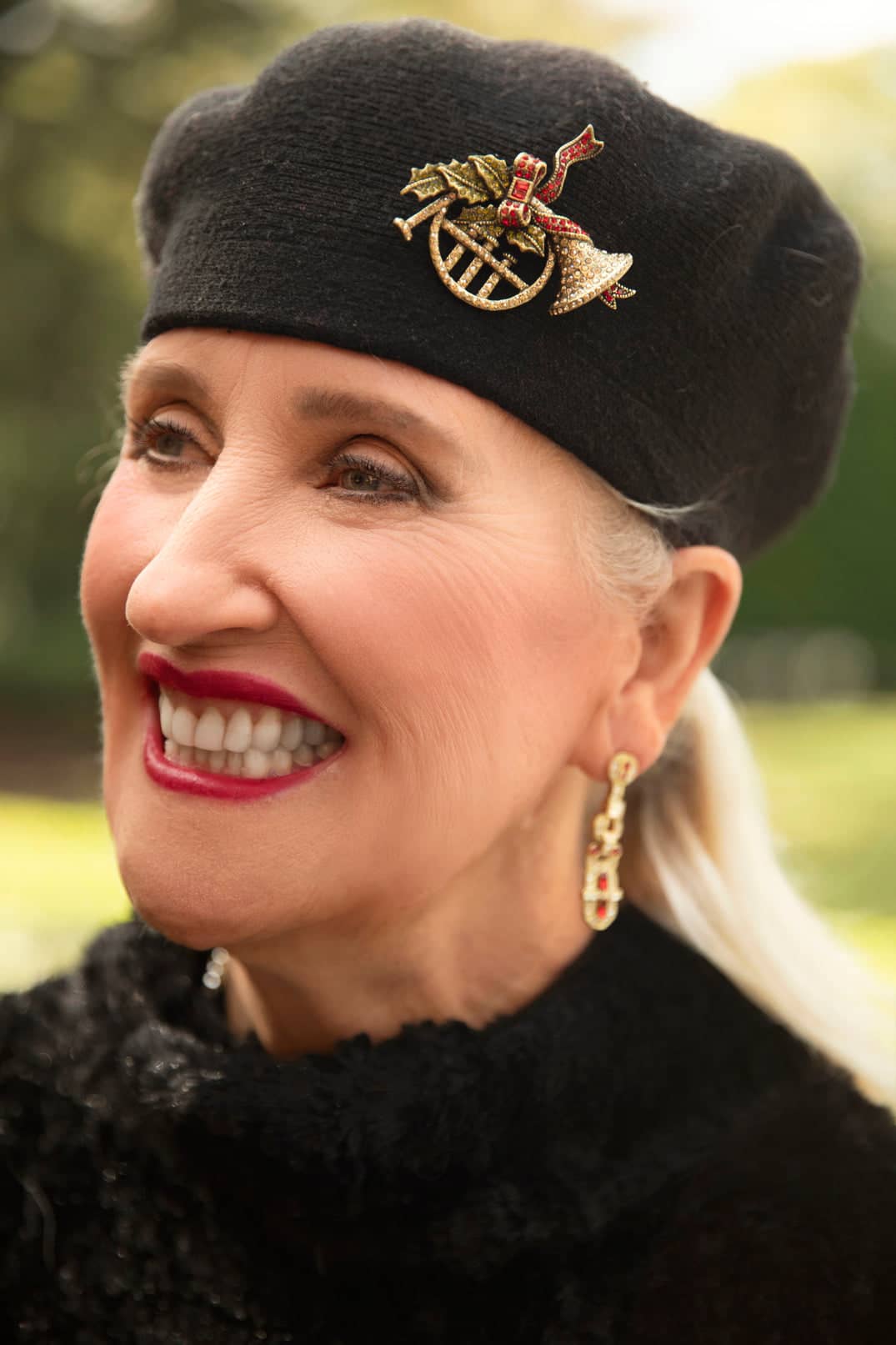 Woman wearing a black beret with a decorative emblem, smiling outdoors.