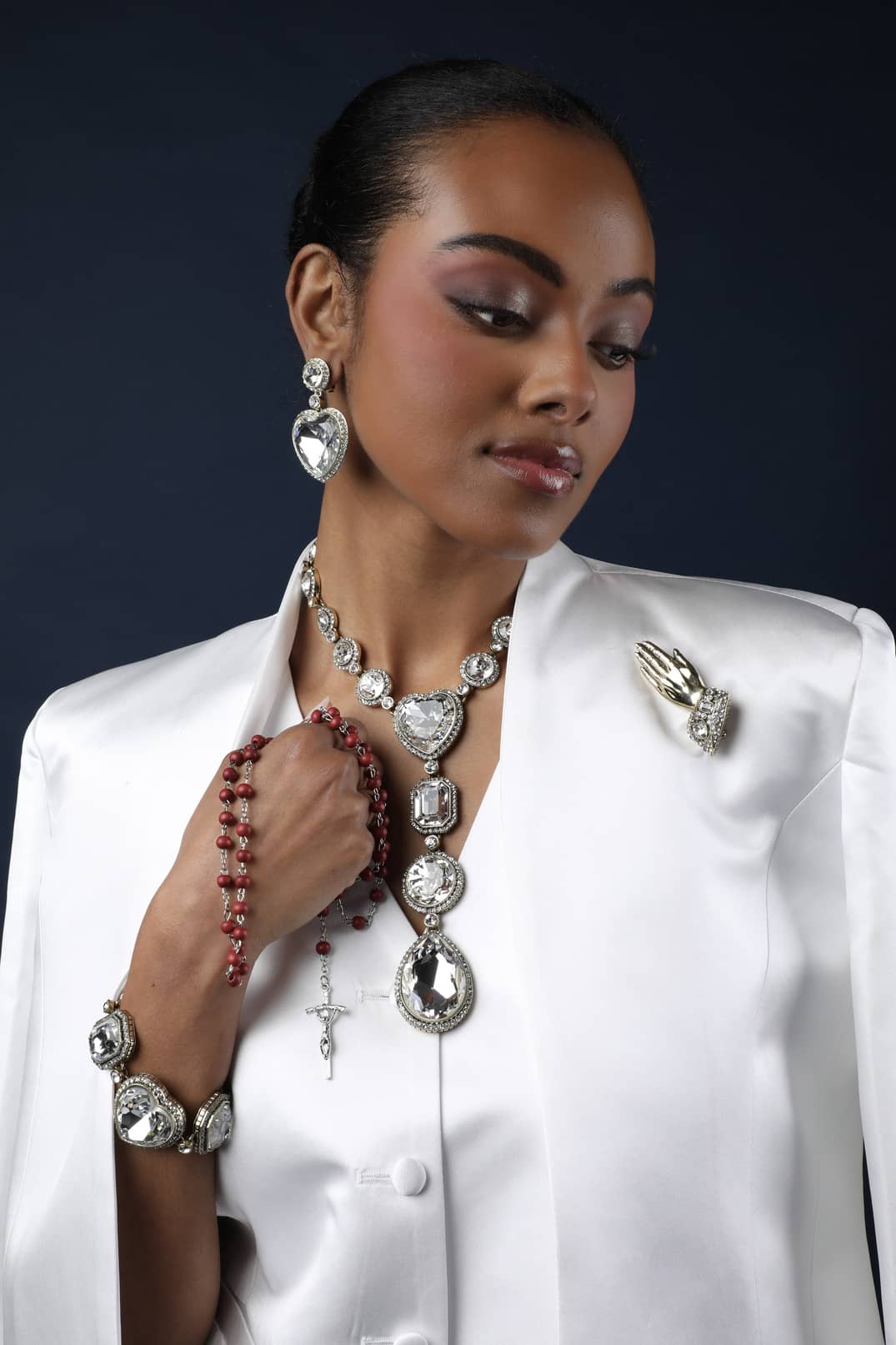 Woman wearing a white outfit with jewelry including a necklace, earrings, and brooch.