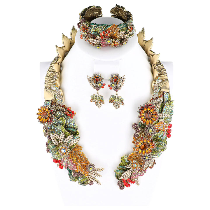 A gold-tone statement jewelry set displayed on a white mannequin bust, featuring a large floral choker necklace, a matching wide bracelet, and two matching drop earrings. The jewelry is heavily embellished with colorful enamel, rhinestones, and floral motifs.