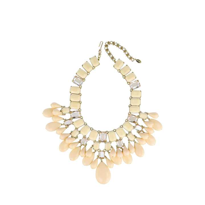 A gold-tone statement bib necklace featuring cream-colored faux shell beads, rectangular and teardrop-shaped elements, and clear rhinestone accents, displayed on a solid white background.
