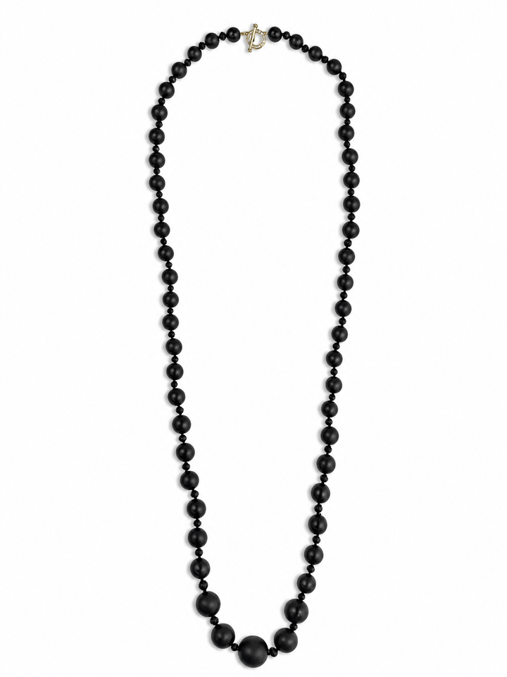 A long black beaded necklace with alternating small and large matte beads, featuring a small gold clasp at the top, displayed on a solid white background.