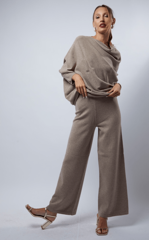Woman wearing a beige outfit with wide-leg pants on a plain background