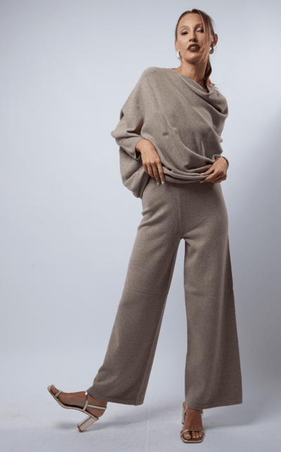 Woman wearing a beige outfit with wide-leg pants on a plain background