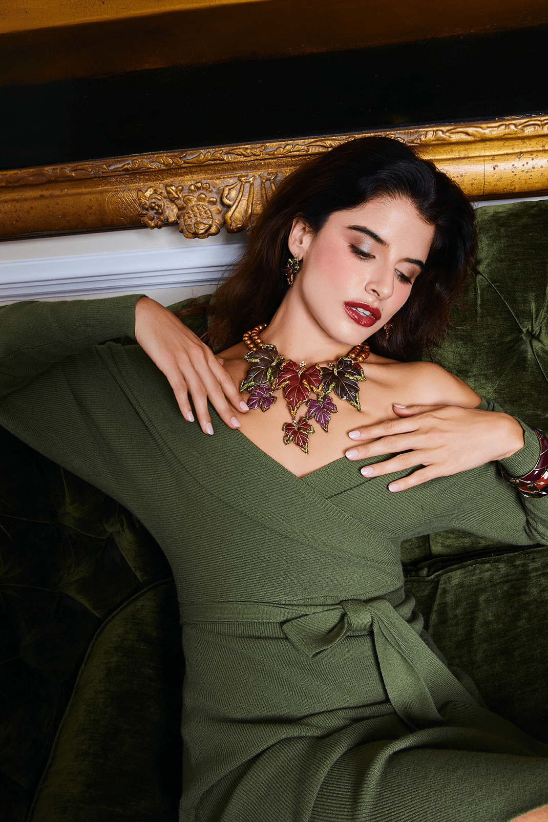 Woman wearing a green dress with a decorative necklace, sitting on a green couch.